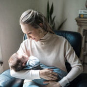 A mother sitting on a chair while gently holding her baby and smiling